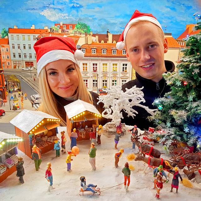 Kobieta i mężczyzna w czapkach mikołajowych na tle świątecznej makiety w Kolejkowie